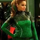 Curly Red-Haired Woman in Green NASA Latex Suit poses confidently