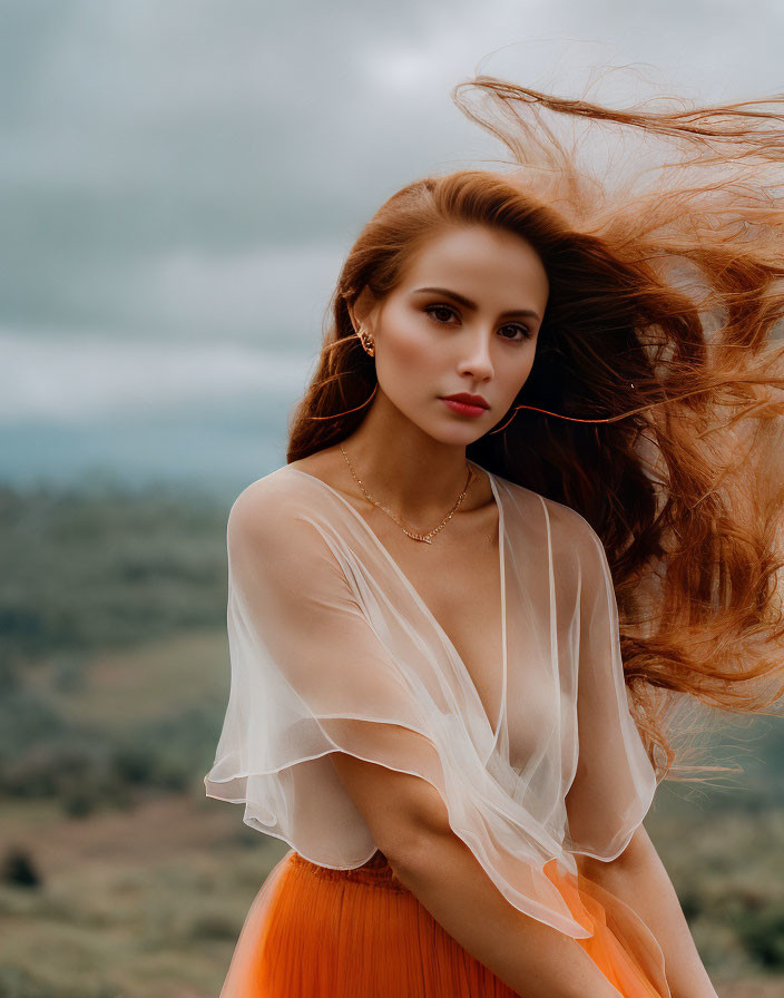 Auburn-haired woman in sheer blouse and orange skirt against cloudy landscape