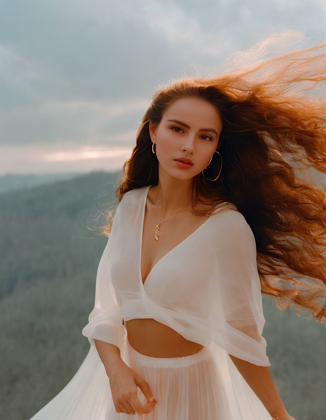 Woman with long flowing hair in sheer white top against dusky sky