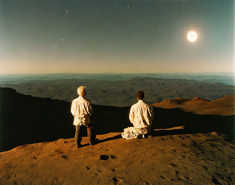 Two People Gazing at Bright Moon Over Rugged Landscape