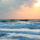 Scenic sunset over turbulent sea with cresting waves under cloudy sky