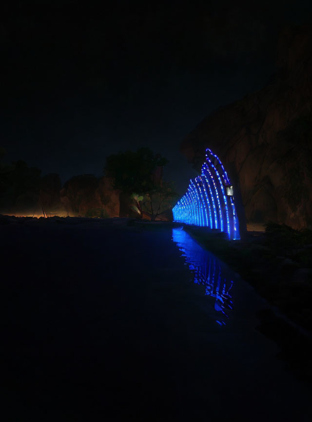 Blue illuminated archway reflected in water near rock formations and solitary tree