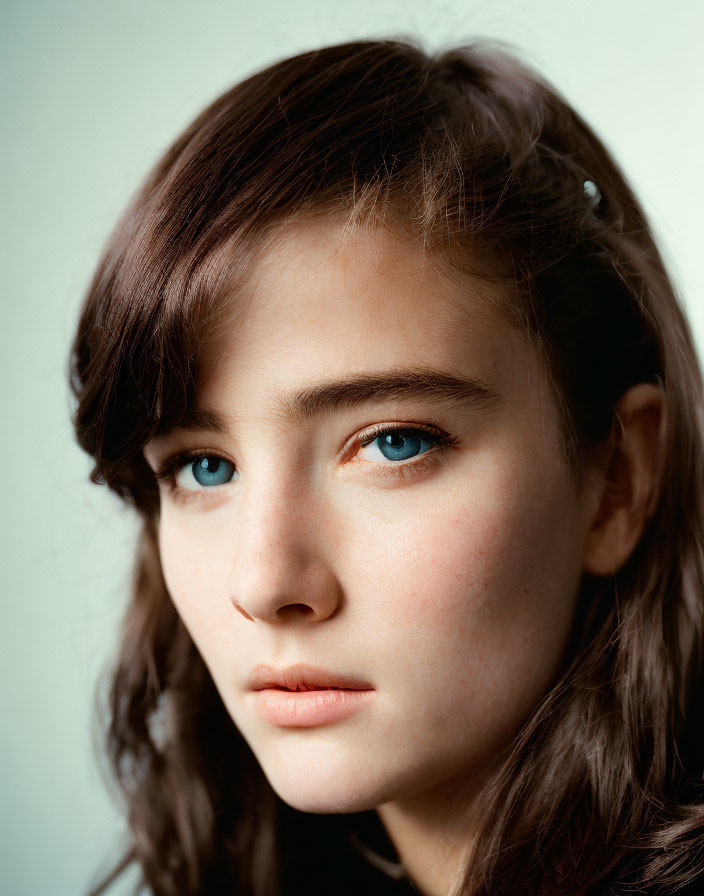 Young woman with blue eyes and brown hair in neutral expression on soft blue background