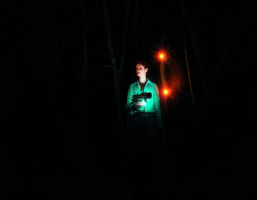 Person standing in dark forest with camera under beam of light and red flare effect