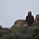 Person standing in desert with rocks and shrubbery under overcast sky