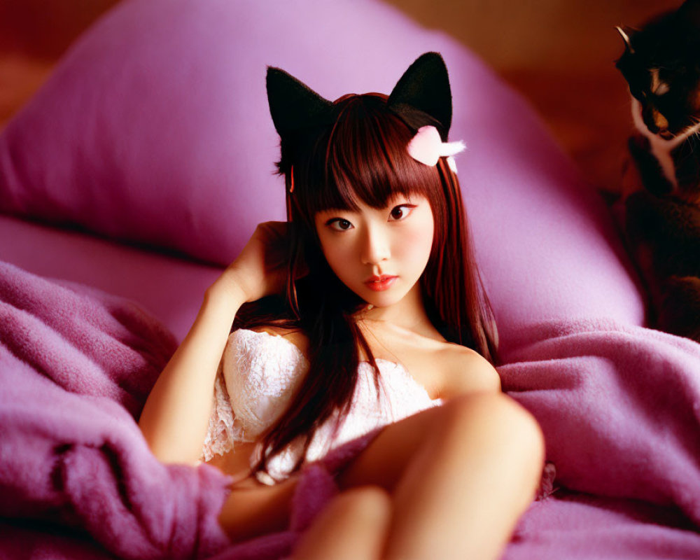 Person wearing cat ears headband reclining on pink beanbag with cat in background