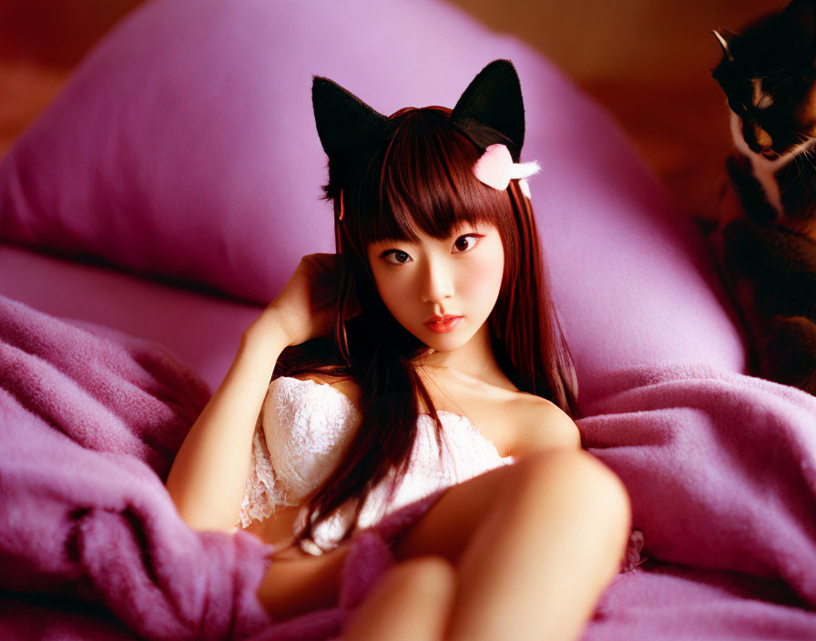 Person wearing cat ears headband reclining on pink beanbag with cat in background