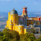 Golden castle with domes and towers in lush landscape with flying birds under blue sky