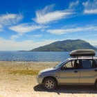 Blue SUV parked on coastal dirt road with clear skies and rocky island.