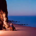 Tranquil beach scene at dusk with person on chair, rocky cliff, and calm ocean waters.