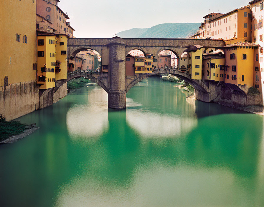 Historic stone bridge over green river with colorful buildings and hills