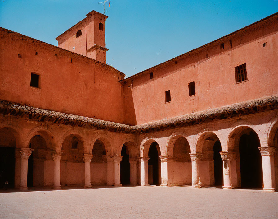 Sunlit courtyard with arcades and bell tower in terracotta building.