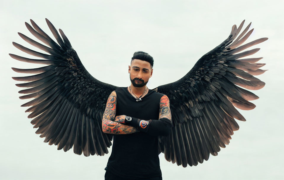 Tattooed man with black artificial wings on cloudy sky background