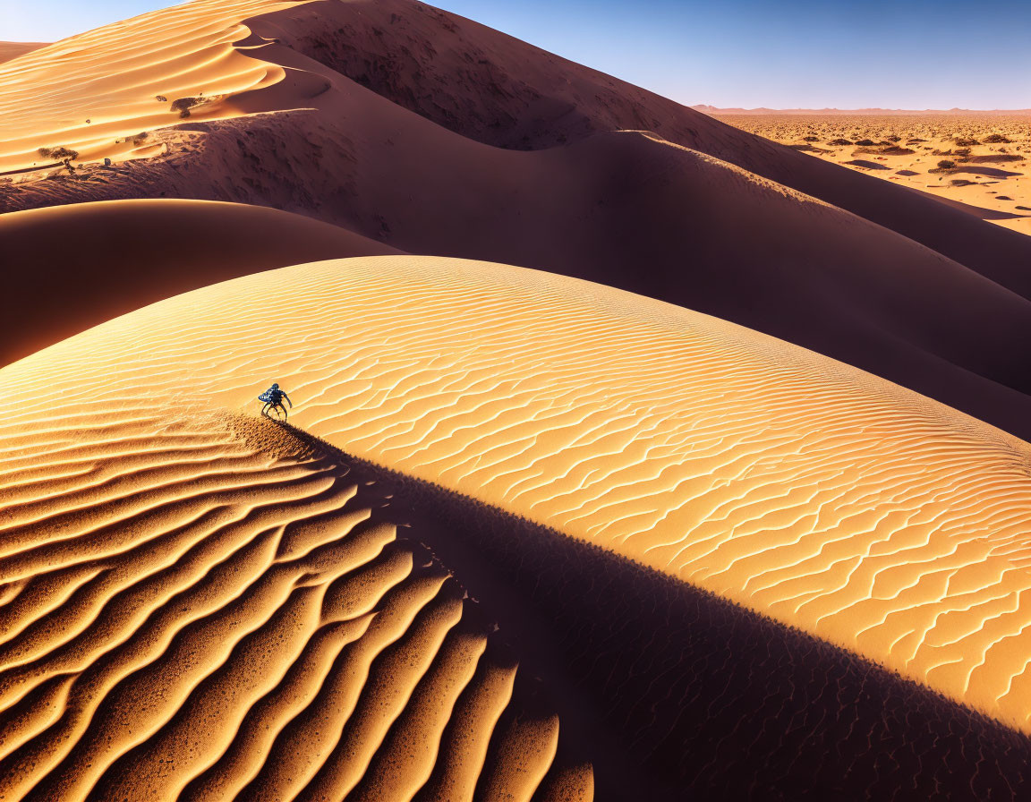 Cyclist on sand dune crest in vast desert with wave patterns.