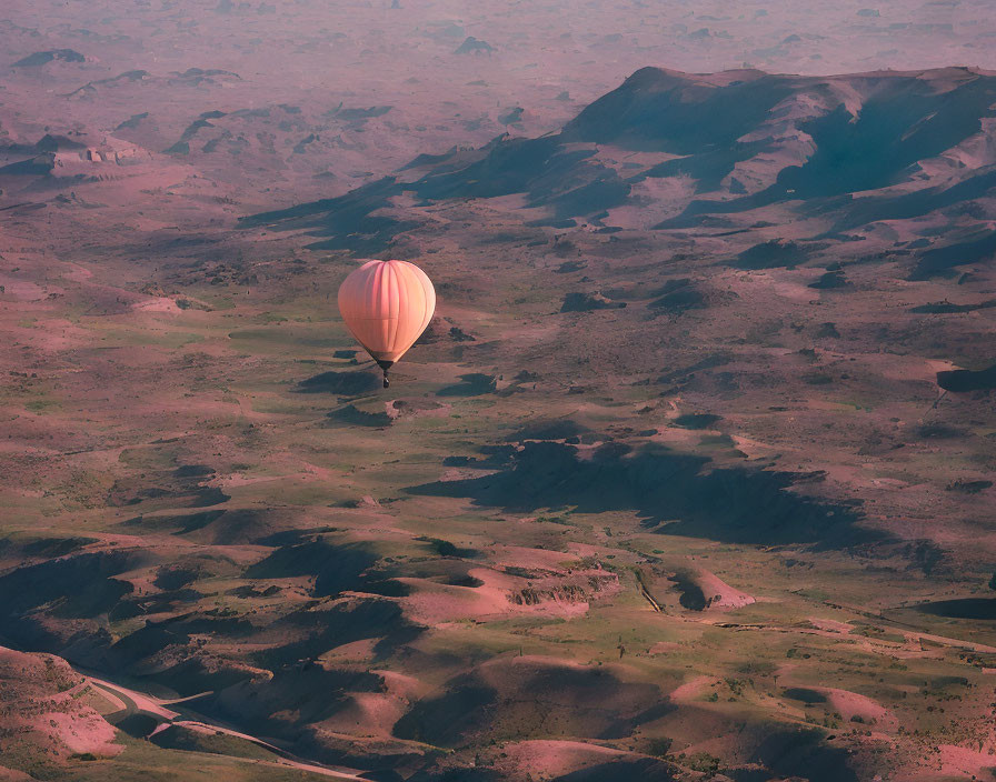 Hot air balloon above rugged landscape at sunrise or sunset
