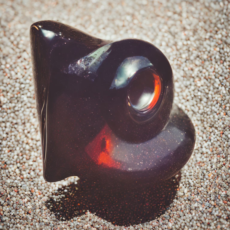 Dark Glass Sculpture with Swirling Form and Red Reflection on Sandy Surface