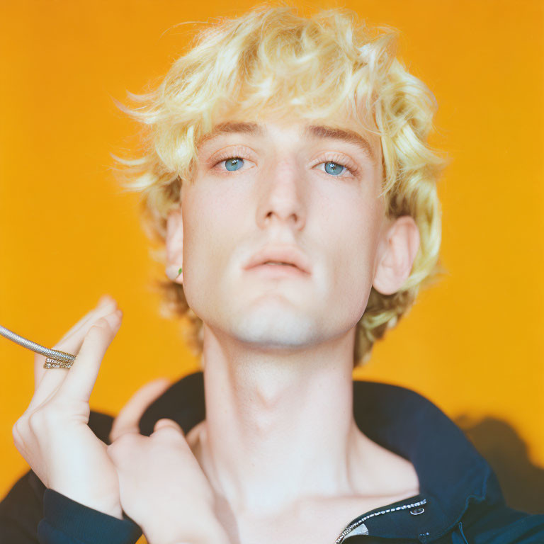 Curly Blond Hair and Blue Eyes Person Holding Pen on Orange Background