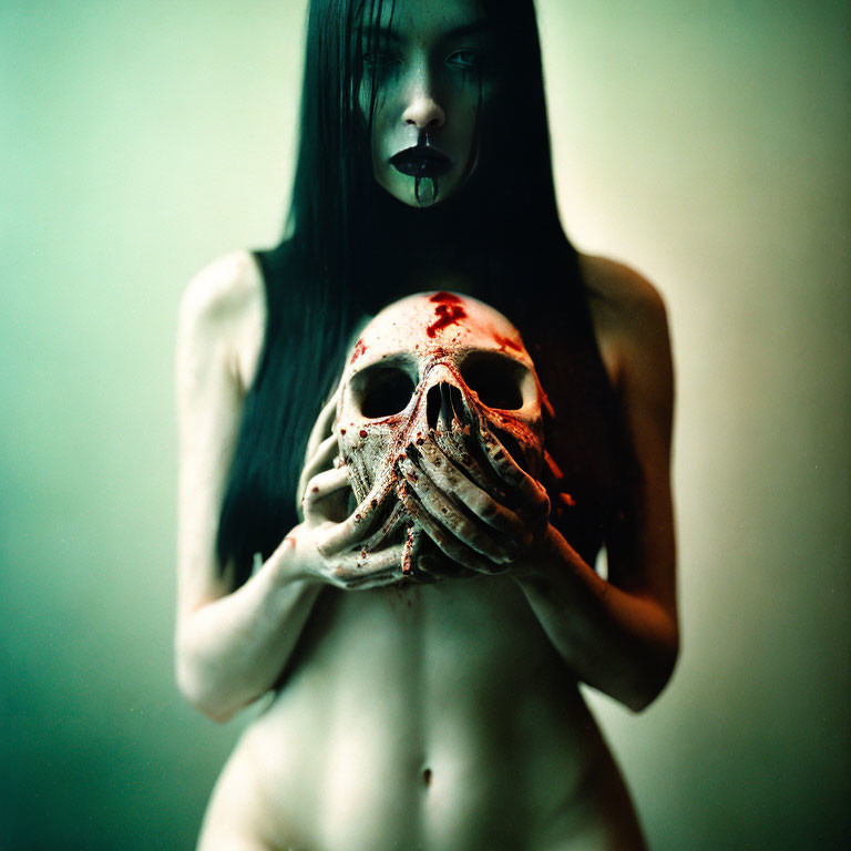 Dark-haired person with pale skin holding blood-stained skull on muted background