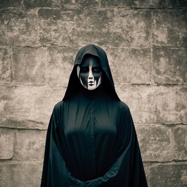 Black Cloaked Figure with White and Black Face Makeup Against Grey Wall