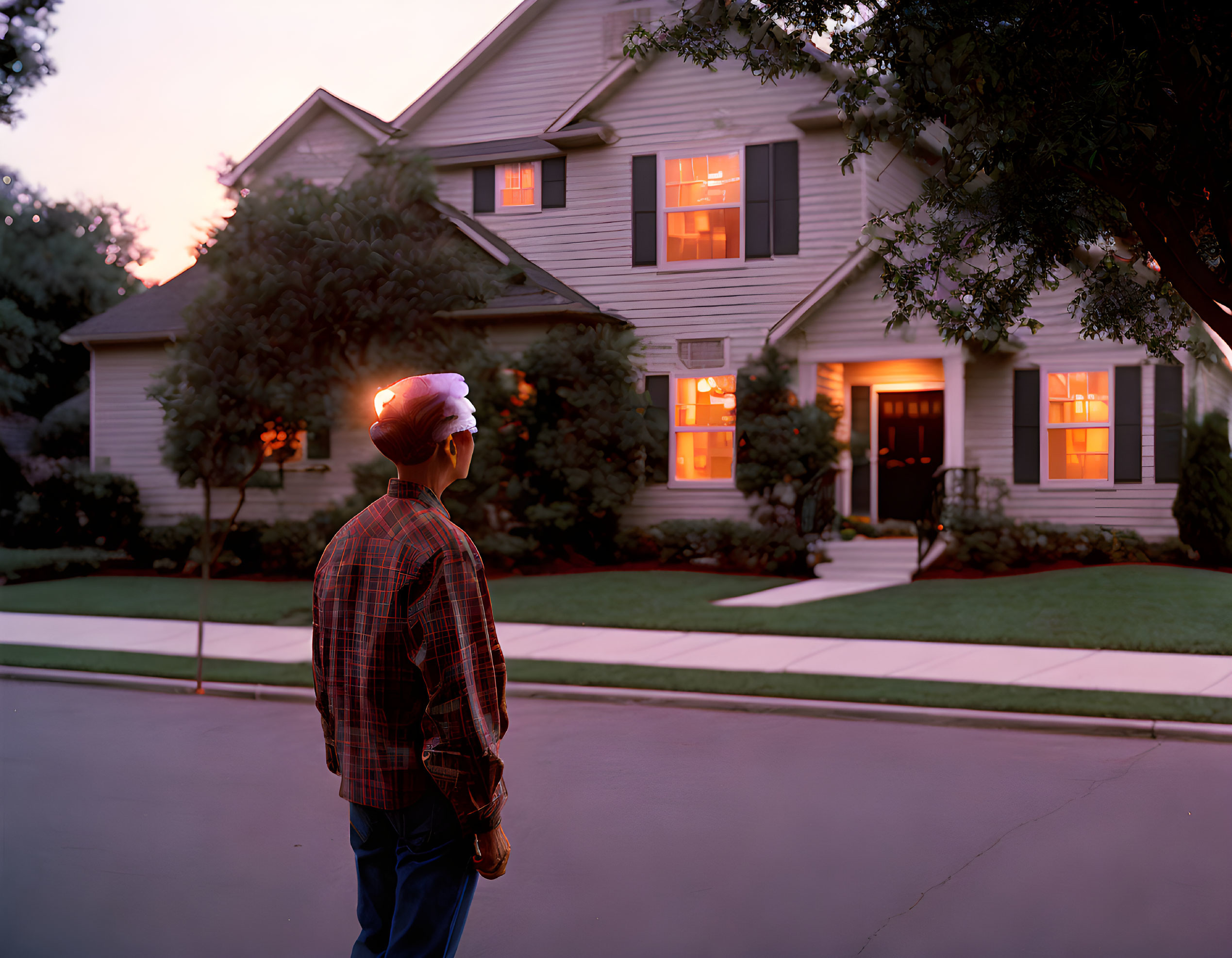 Man in Plaid Shirt Standing by Two-Story House at Dusk