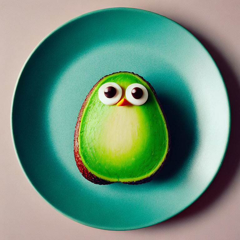 Cartoonish avocado with googly eyes on teal plate against pink background