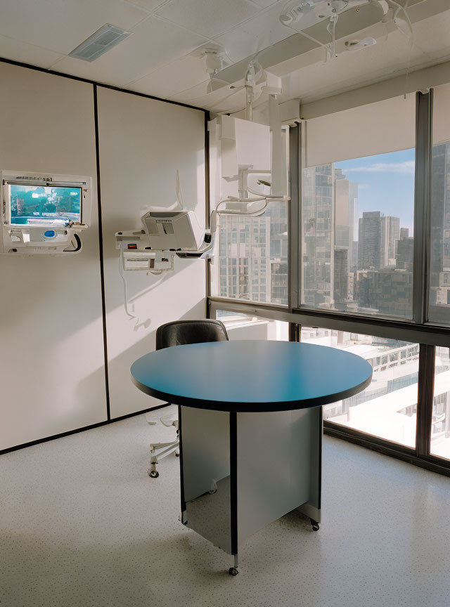 Hospital room with medical equipment, round table, chair, and cityscape view