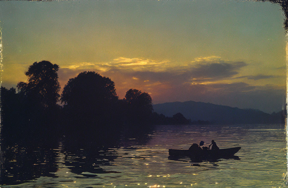 Silhouette of person rowing boat on calm river at sunset