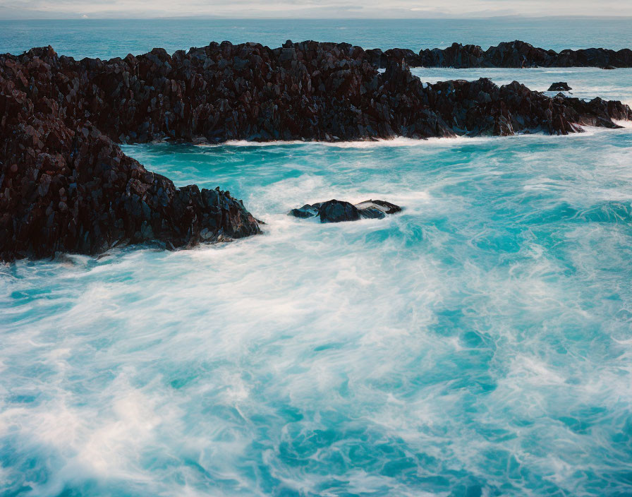 Swirling Turquoise Ocean Waves Around Jagged Black Rocks