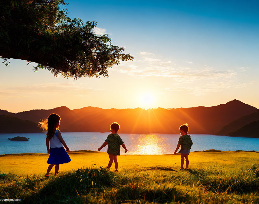 Children playing under tree at sunset near sea and mountains.