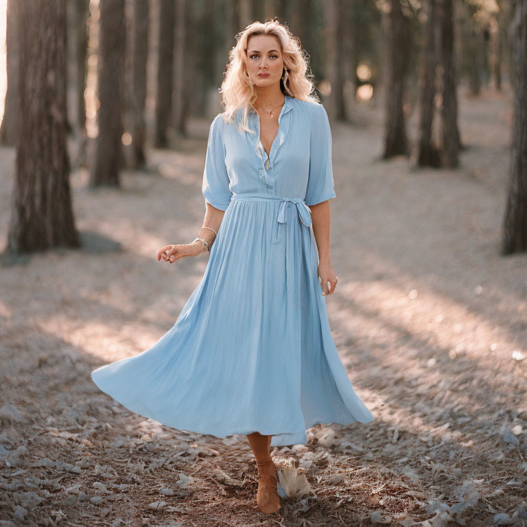 Woman in flowing blue dress in sun-dappled forest with blond hair and simple jewelry.