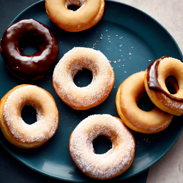 Assorted glazed and sugar-topped donuts on dark blue plate