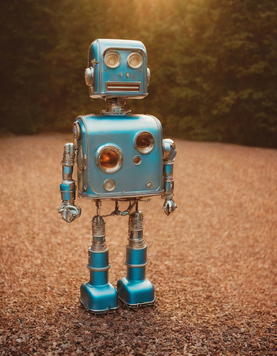 Blue vintage-style robot with square head and circular eyes on gravel surface.