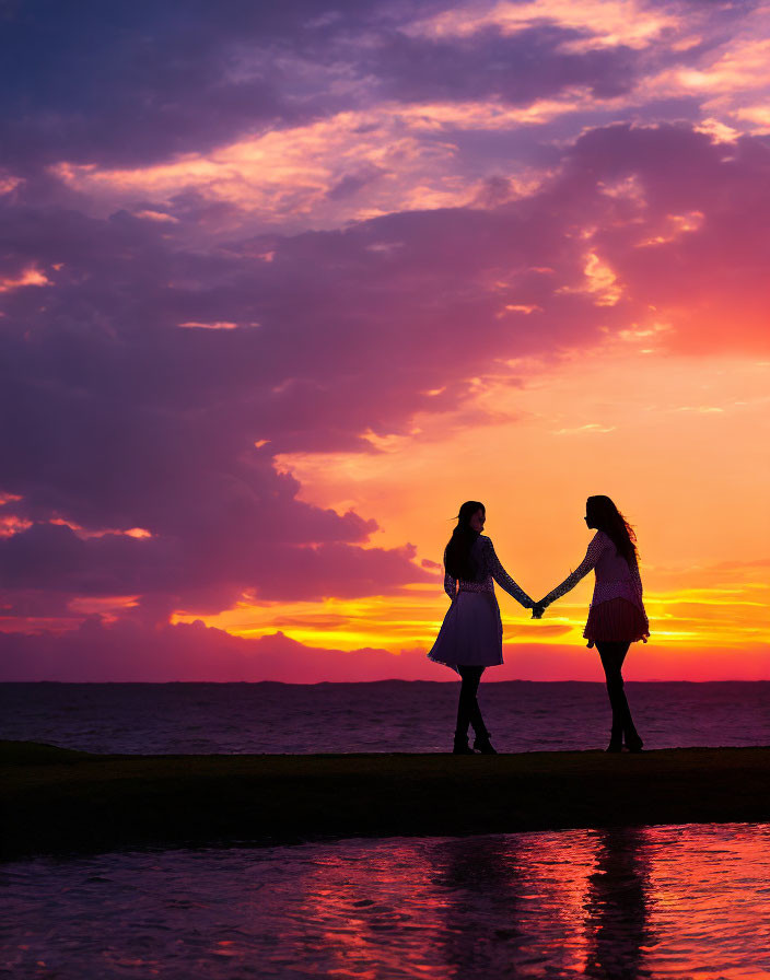 Silhouetted individuals holding hands at vibrant sunset over calm sea