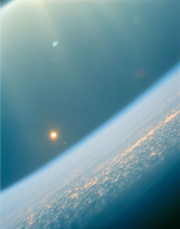 Sunlight creating lens flare over Earth's curved horizon with city lights below