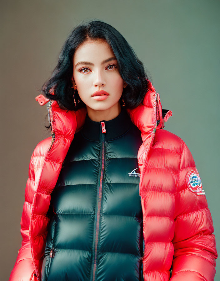Dark-haired woman in red and black puffer jacket on neutral backdrop