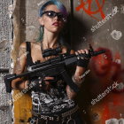 Vibrant woman with colorful hair and tattoos holding a rifle in a leather jacket.
