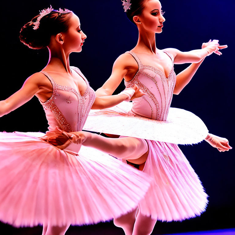 Two ballet dancers in pink tutus and tiaras pose against a deep blue background