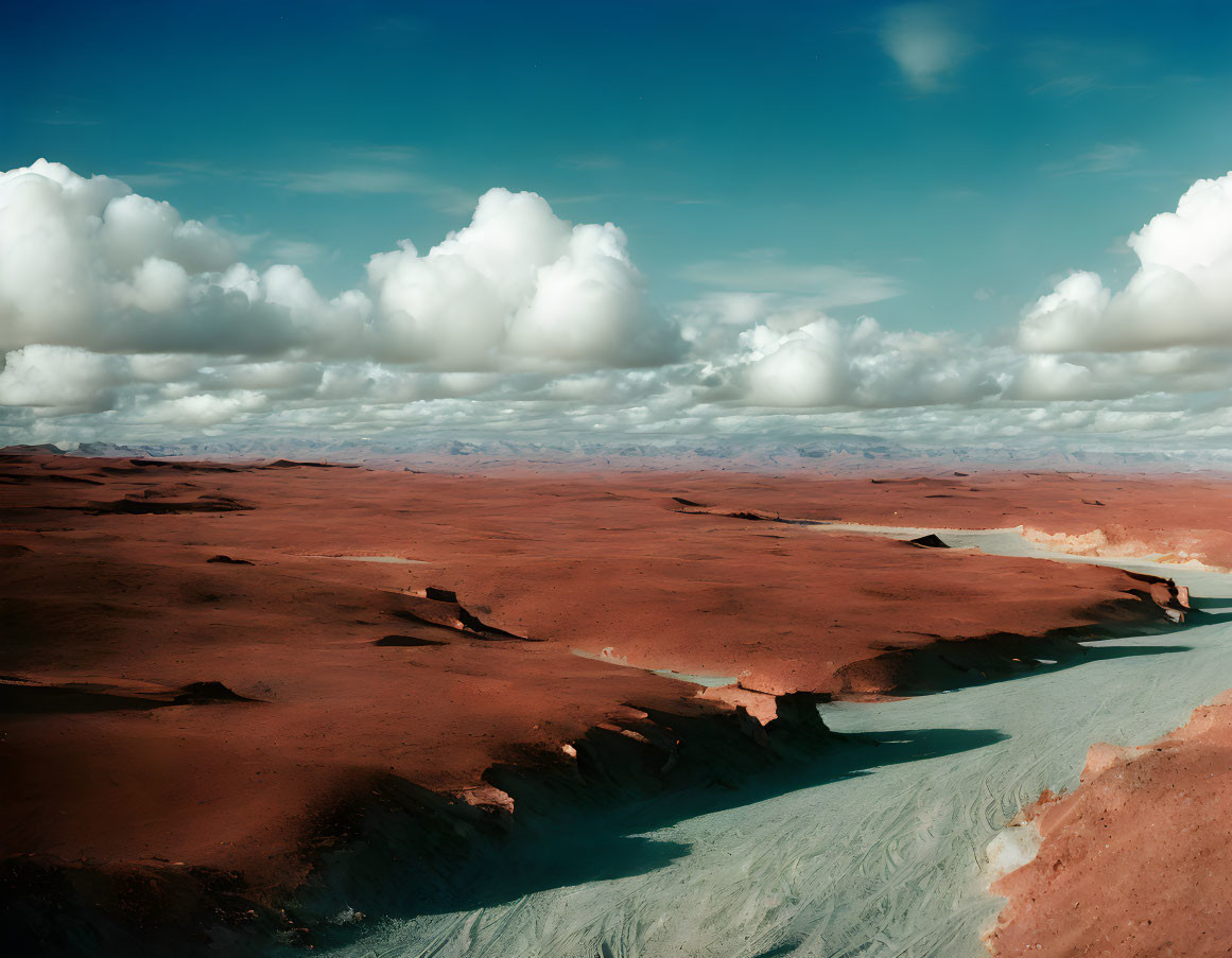 Tranquil desert scene: red sand dunes, blue sky, white clouds, and winding river