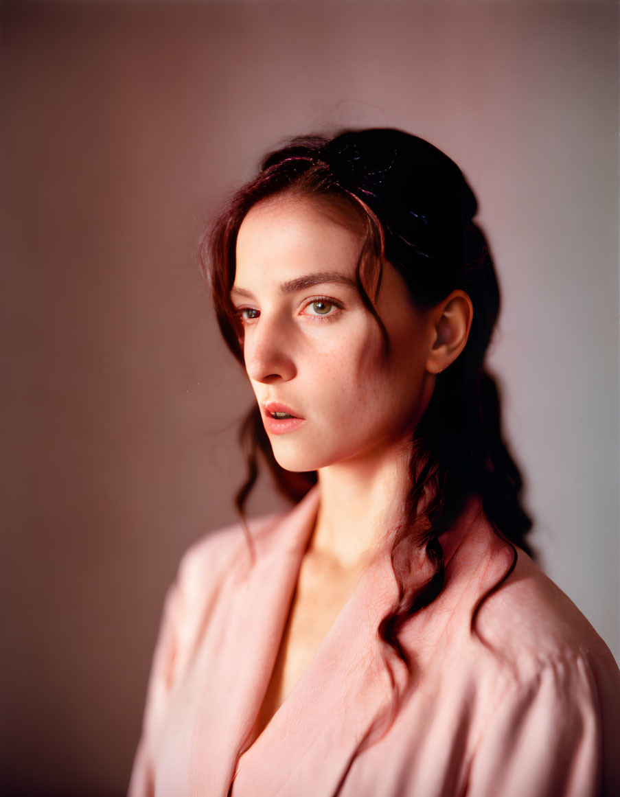 Dark-haired woman in braids wearing pink outfit gazes at camera in soft light