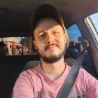 Man in pink shirt with seatbelt in car under sunlight.