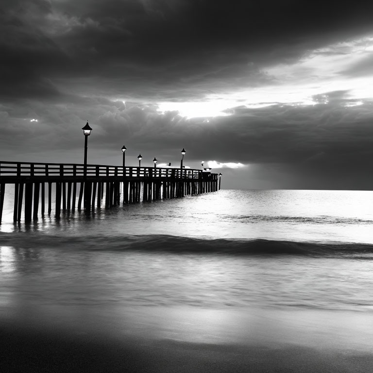 Monochrome image of calm sea with pier and lampposts under dramatic sky