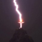 Giant illuminated statue on hilltop with lightning bolts in night sky
