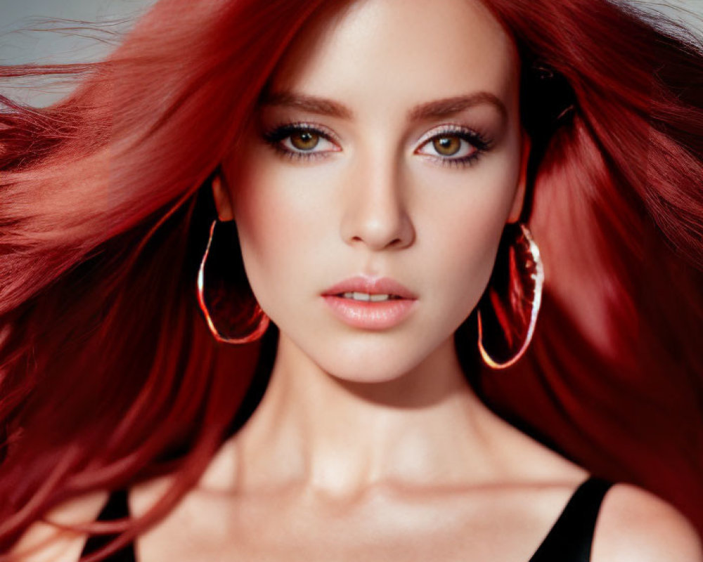Portrait of woman with red hair and green eyes in black top and gold earrings