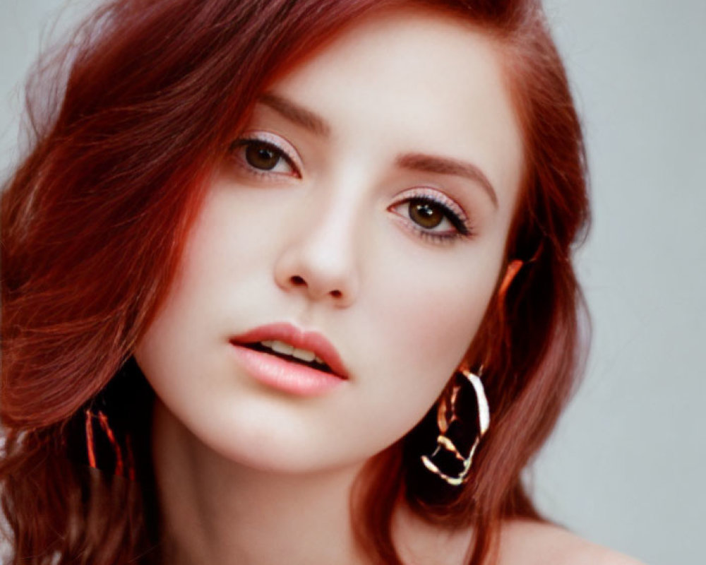 Red-haired woman with hoop earrings in subtle makeup on neutral background