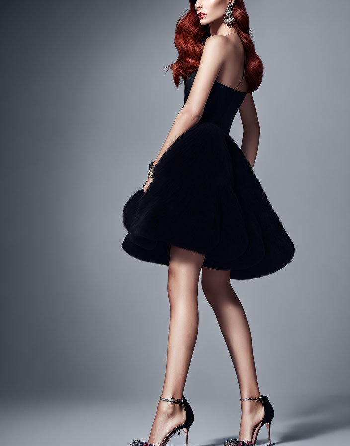 Red-haired woman in black dress and heels poses elegantly on gray background