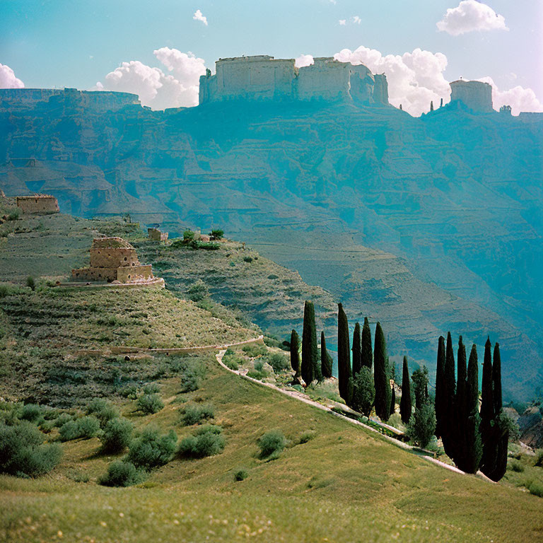 Green hillside with cypress trees & ancient fortress ruins under blue sky
