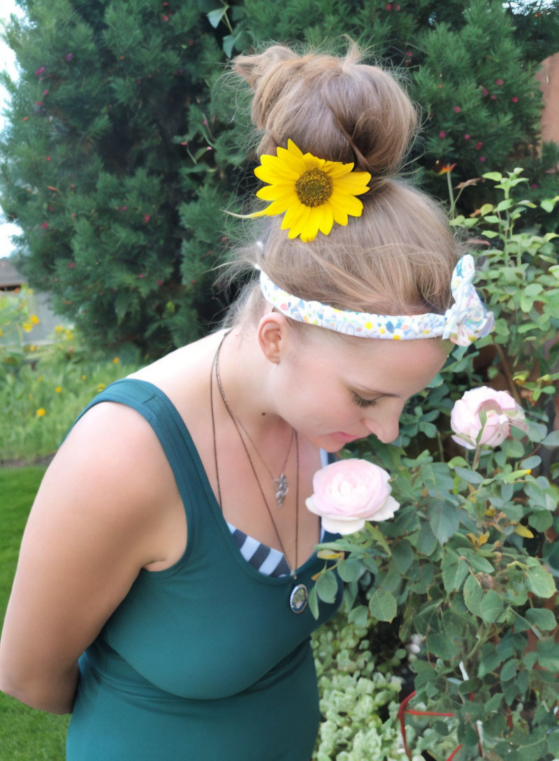 Woman with Sunflower in Hair Bun Smelling Pink Rose in Garden
