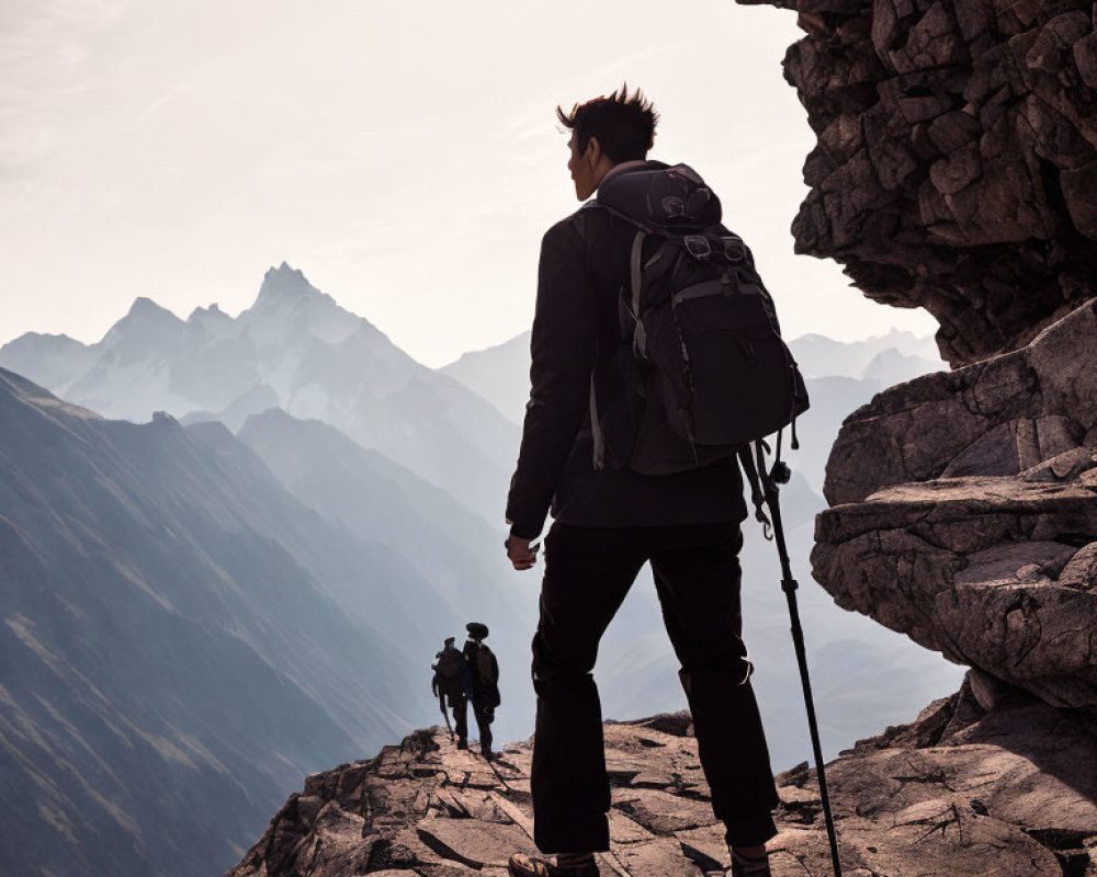 Hiker with backpack on mountain ridge overlooking sharp peaks