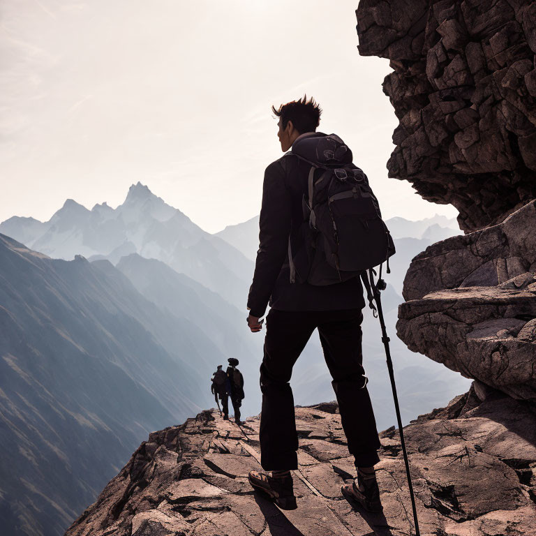 Hiker with backpack on mountain ridge overlooking sharp peaks