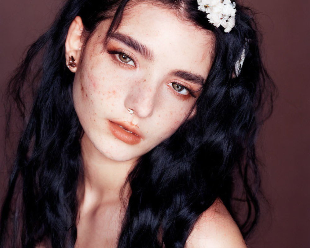 Portrait of person with freckles in white floral headband and nose ring on brown background